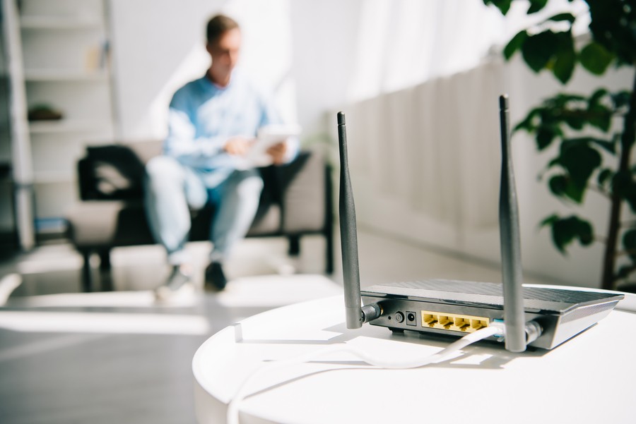 A close-up of a modem while a man uses his tablet in the background.